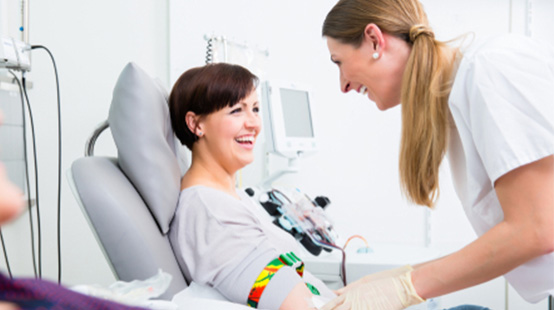 Smiling middle-aged woman donating blood at a Blood Bank of Delmarva with smiling phlebotomist attending to her.