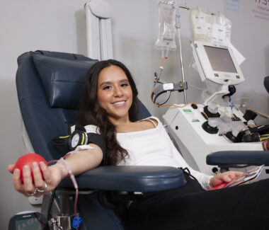 Smiling blood donor in donation chair squeezing a red foam heart.